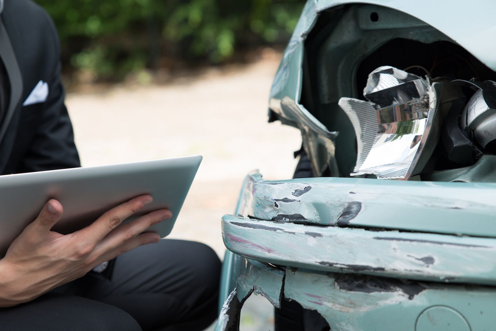 Mann im Anzug kontrolliert mit einem Klemmbrett ein kaputtes Auto